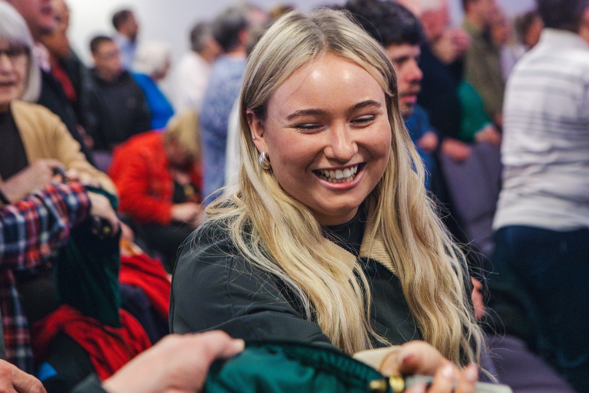 A young woman smiling as people greet one another during worship
