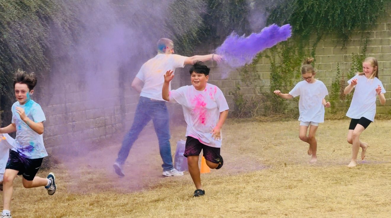 Children and adults running through clouds of coloured powder on the grass during a colour run